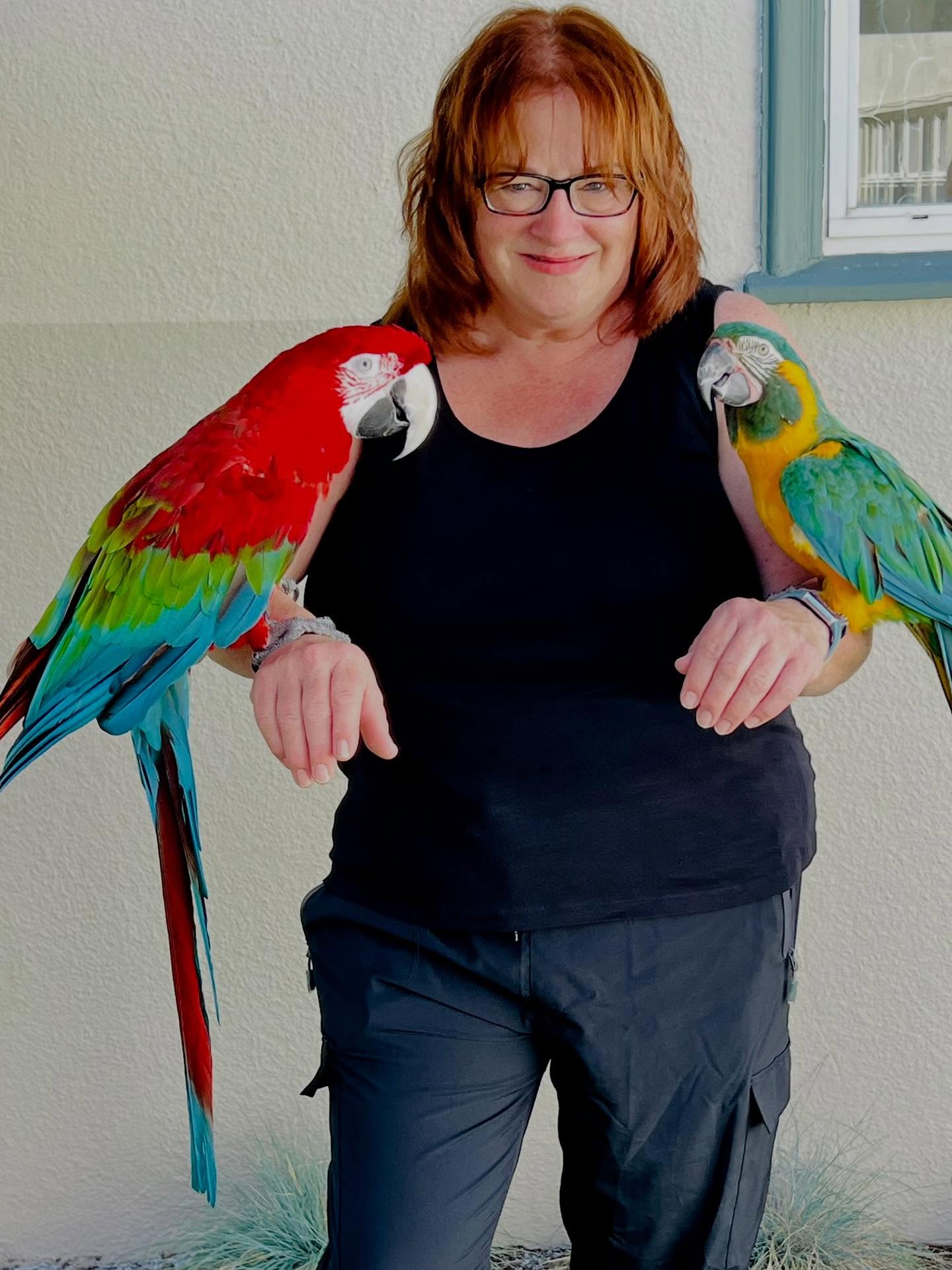 Vikki Gomez, Master Teacher at UMC Preschool, with two colorful parrots